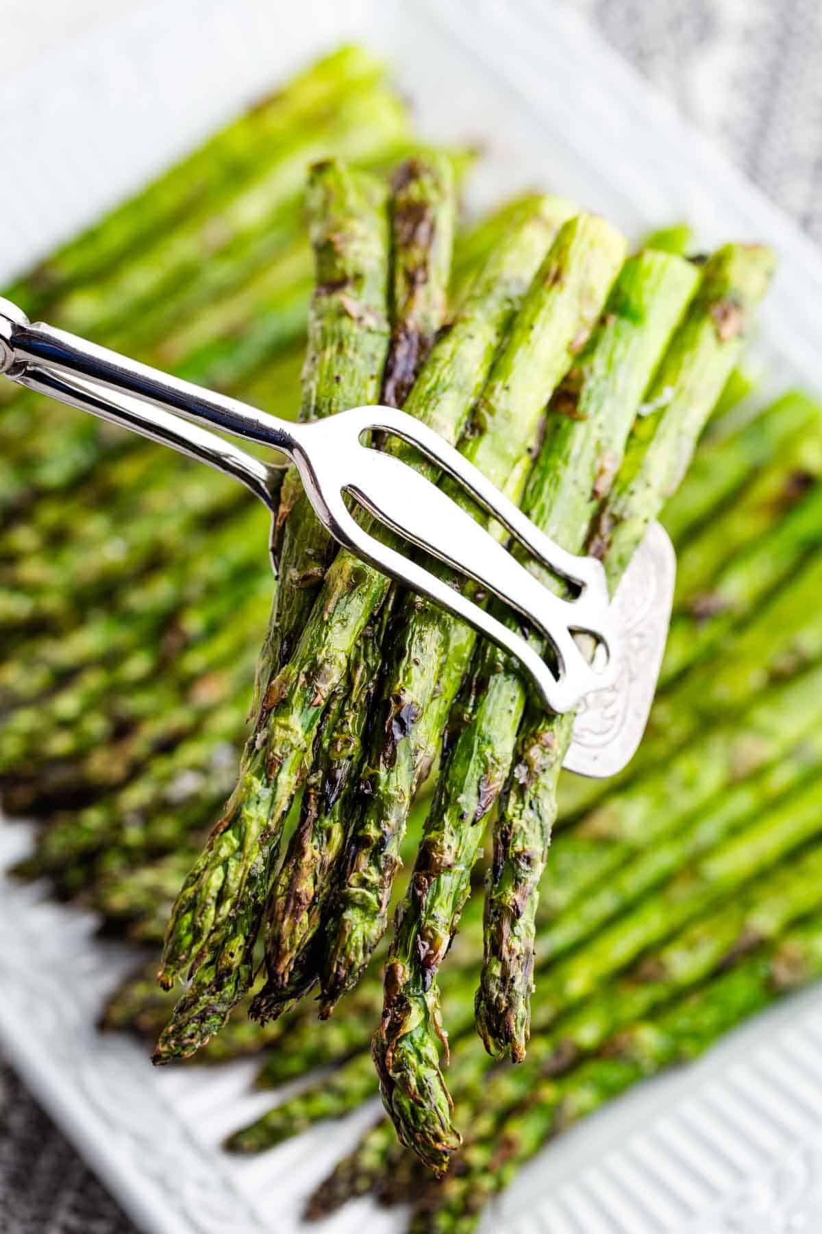 Serving tongs pick up grilled asparagus.