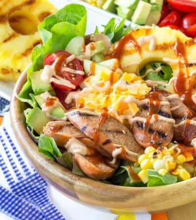 A bowl of chicken sausage salad topped with hot sauce.