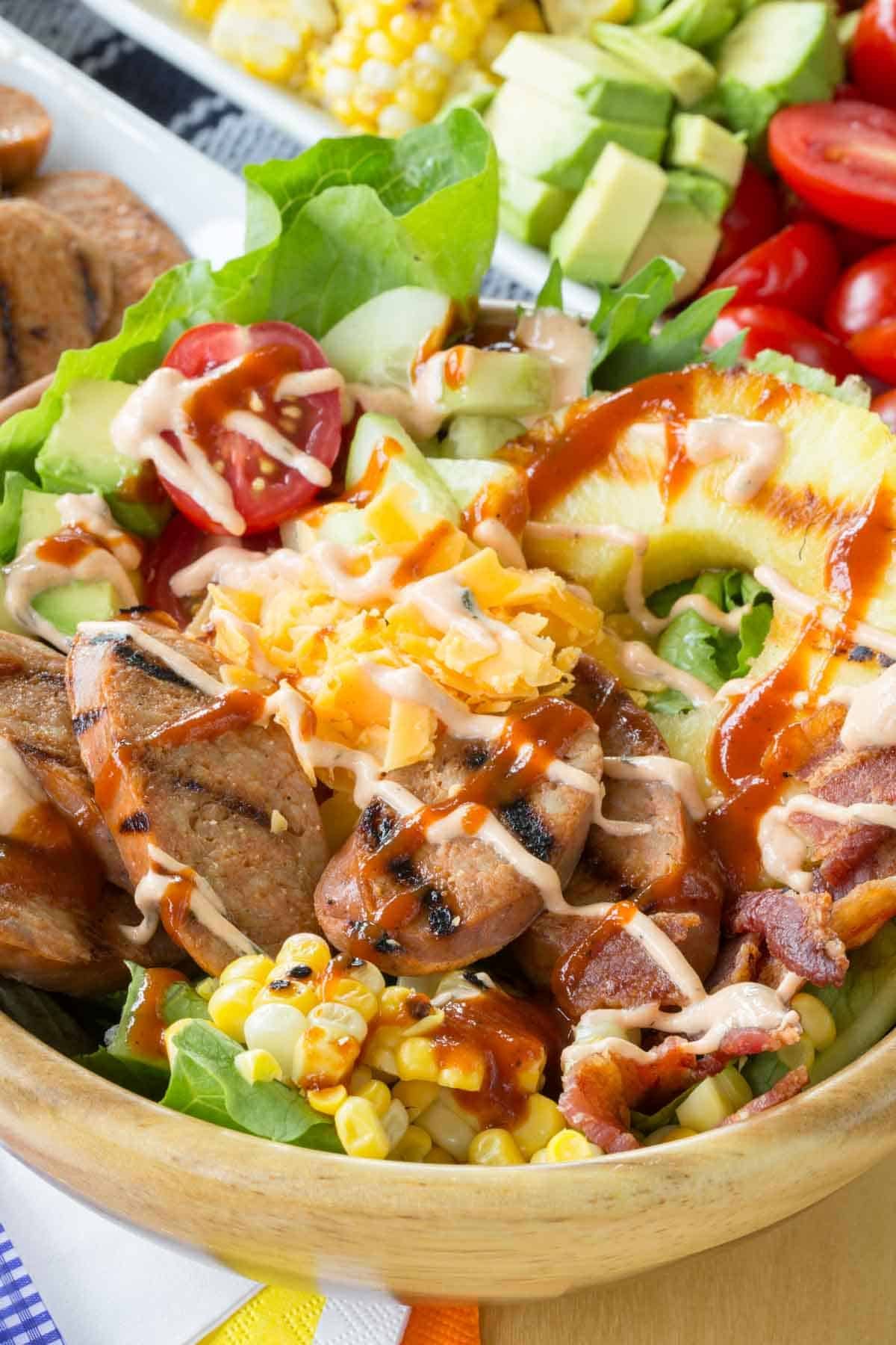 Hot sauce is drizzled over a bowl of grilled chicken sausage salad.