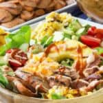 A bowl of chicken sausage salad topped with hot sauce.
