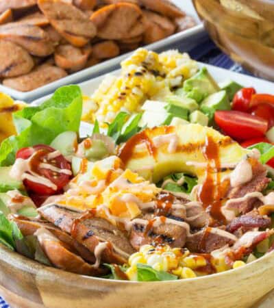 A bowl of chicken sausage salad topped with hot sauce.