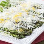 Grilled asparagus on a plate is layered with cheese and lemon zest.
