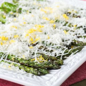 Grilled asparagus on a plate is layered with cheese and lemon zest.