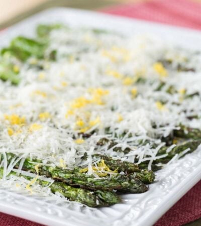 Grilled asparagus on a plate is layered with cheese and lemon zest.