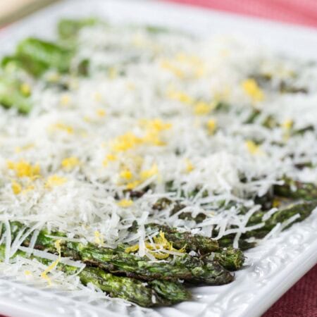Grilled asparagus on a plate is layered with cheese and lemon zest.