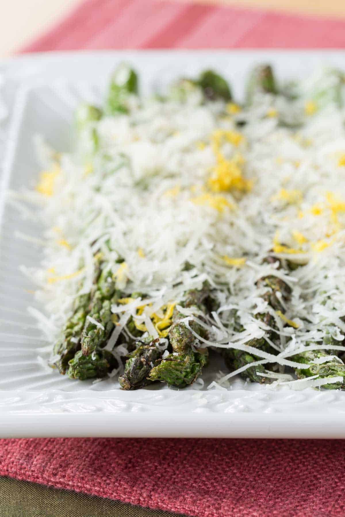 A plate of grilled asparagus topped with melted Parmesan and lemon zest.