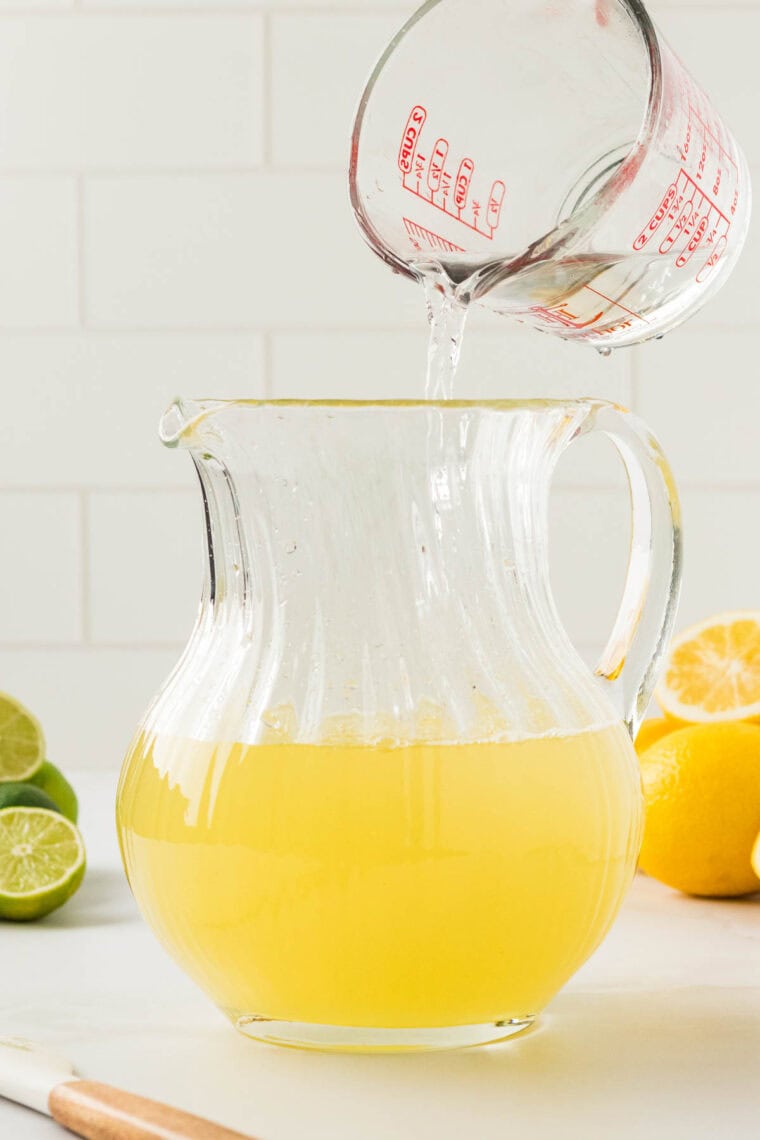 Water is poured into a pitcher of lemon and lime juices.