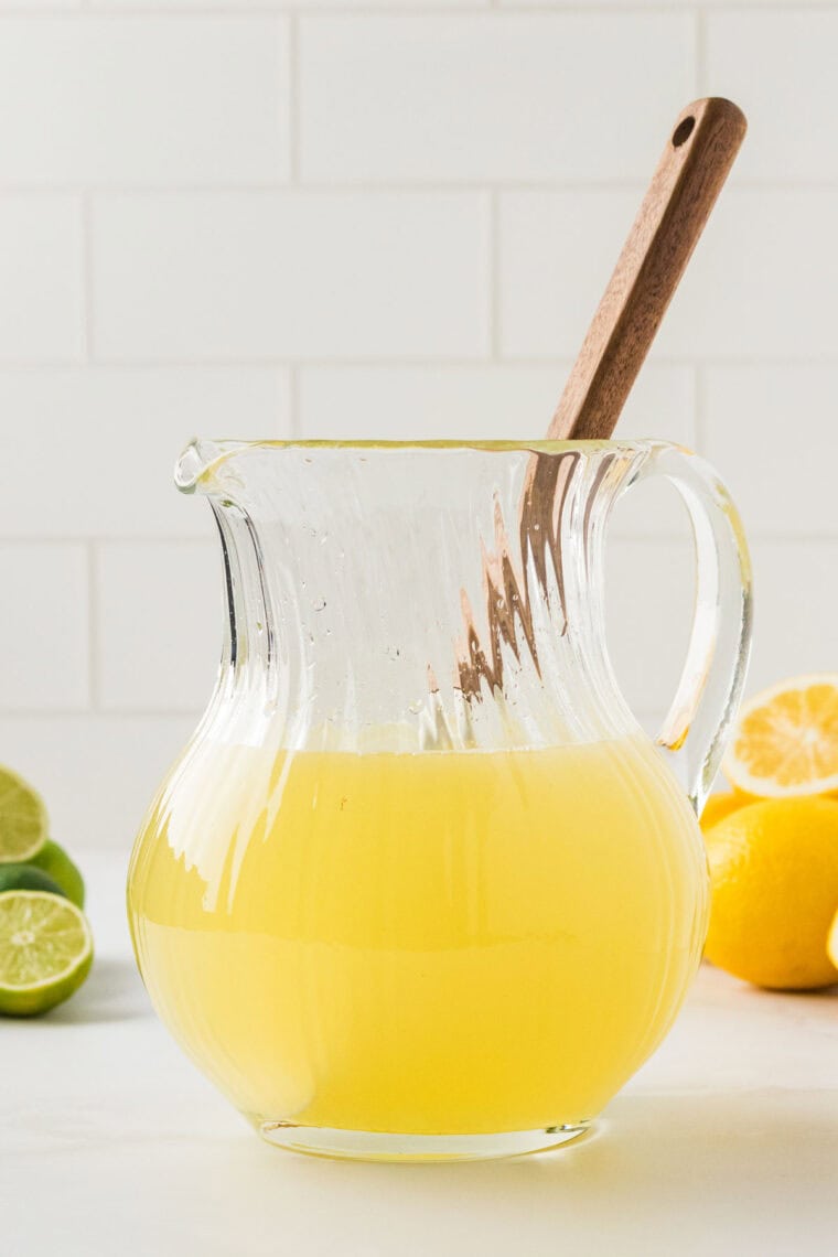 A spoon stirs a glass pitcher of lemon limeade.