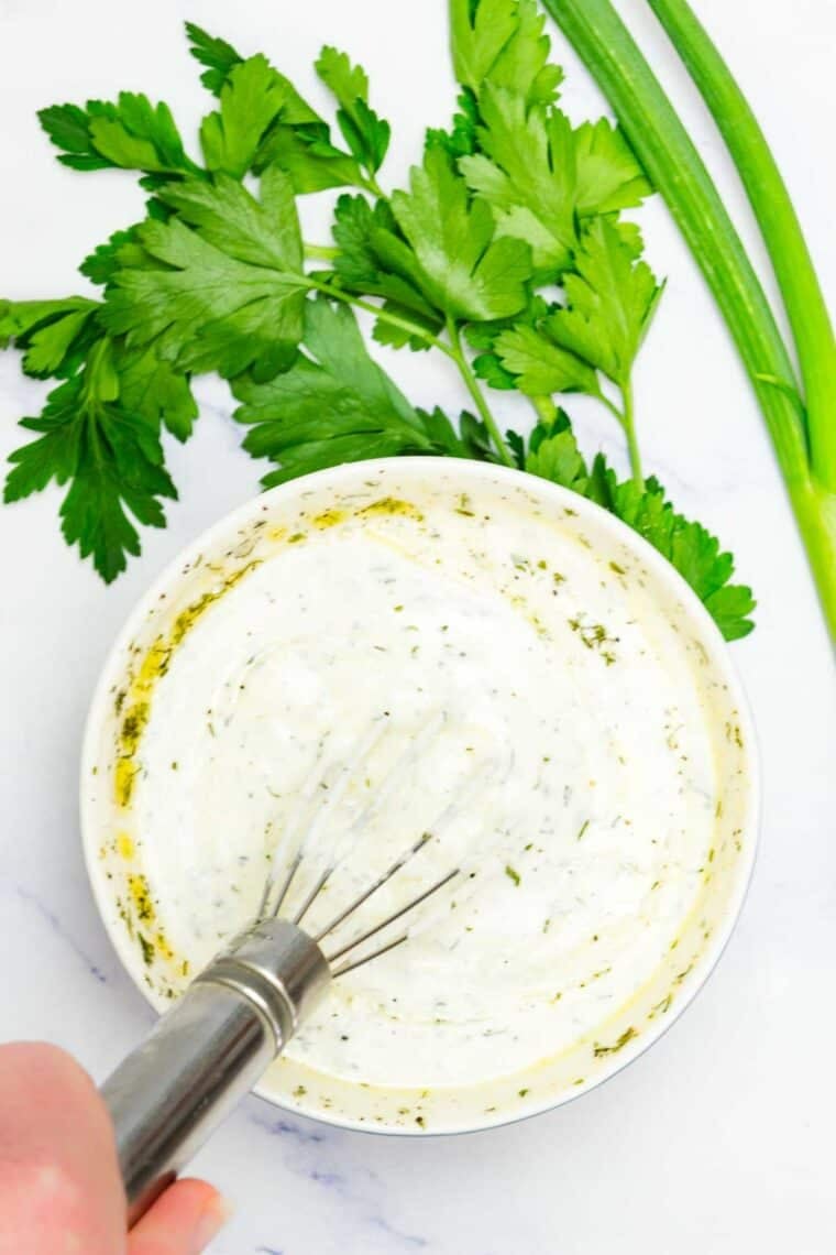 A whisk is used to mix together ranch dressing in a bowl.