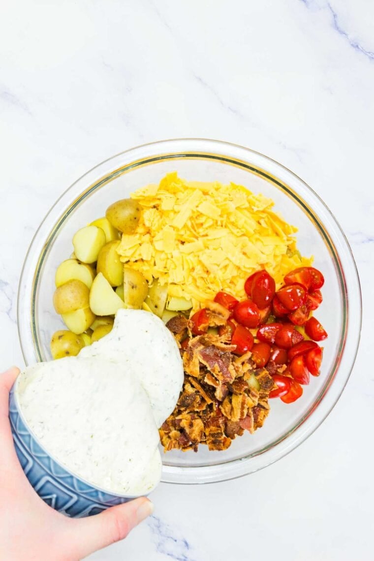 Dressing is poured into a bowl of ranch potato salad.