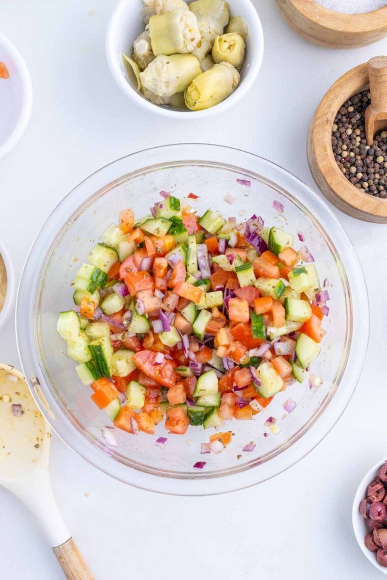 Tossing tomatoes, cucumber, and red onion together with olive oil, lemon juice, and seasonings.
