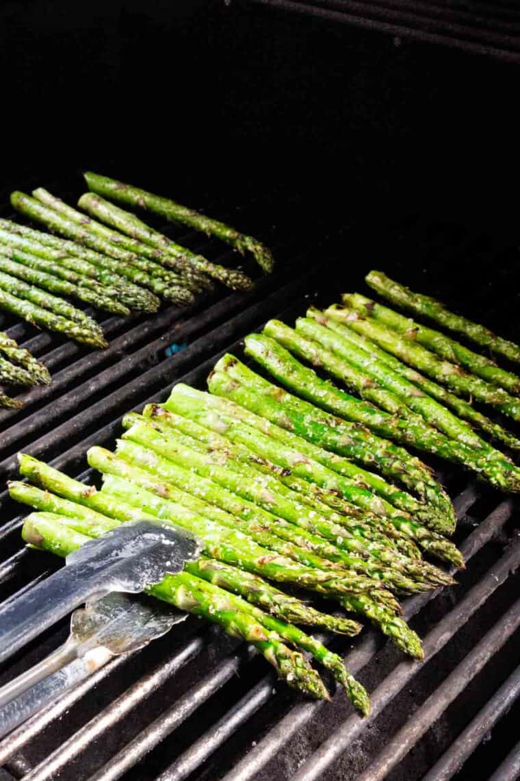 Tongs turn asparagus on the grill.