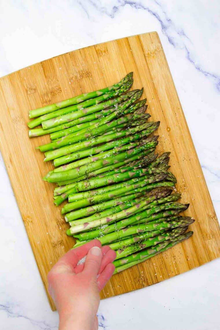Salt and pepper is added to asparagus.