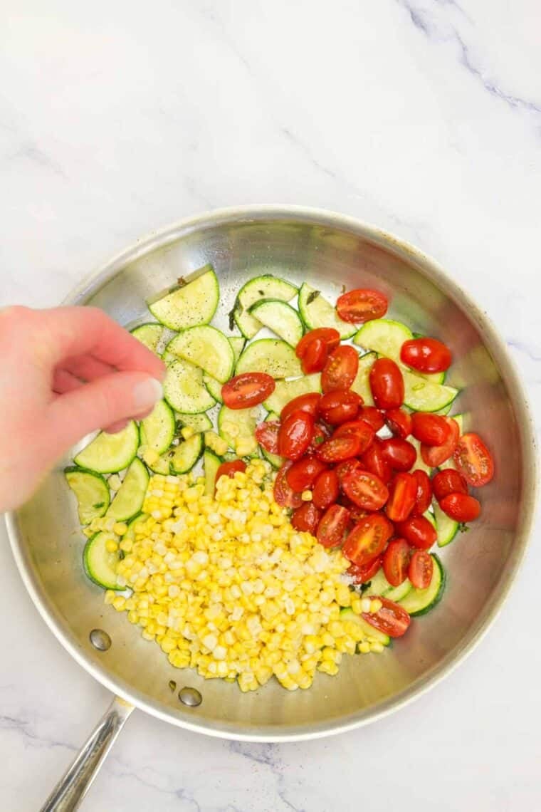 Seasoning is added to a pan of sauteed vegetables.