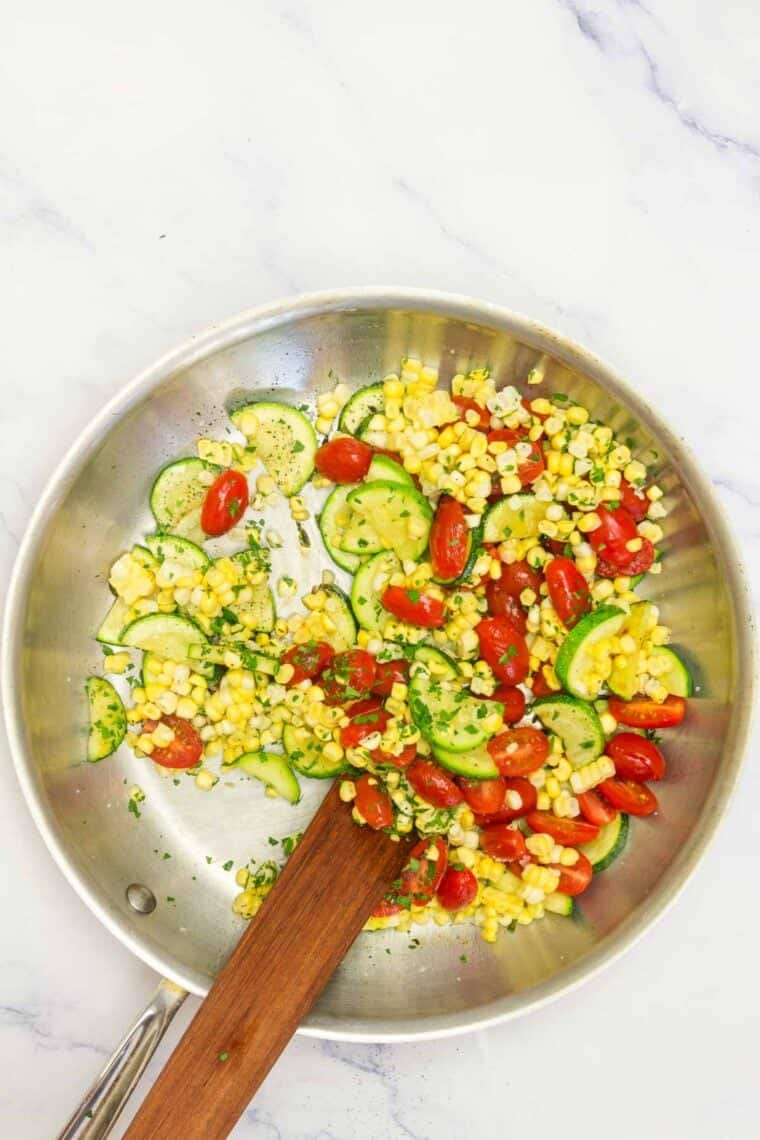 A wooden spoon mixed together sauteed vegetables in a pan.