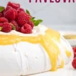 A meringue shell on a platter topped with lemon curd, whipped cream, and berries with text overlay that says "Lemon Curd Pavlova".