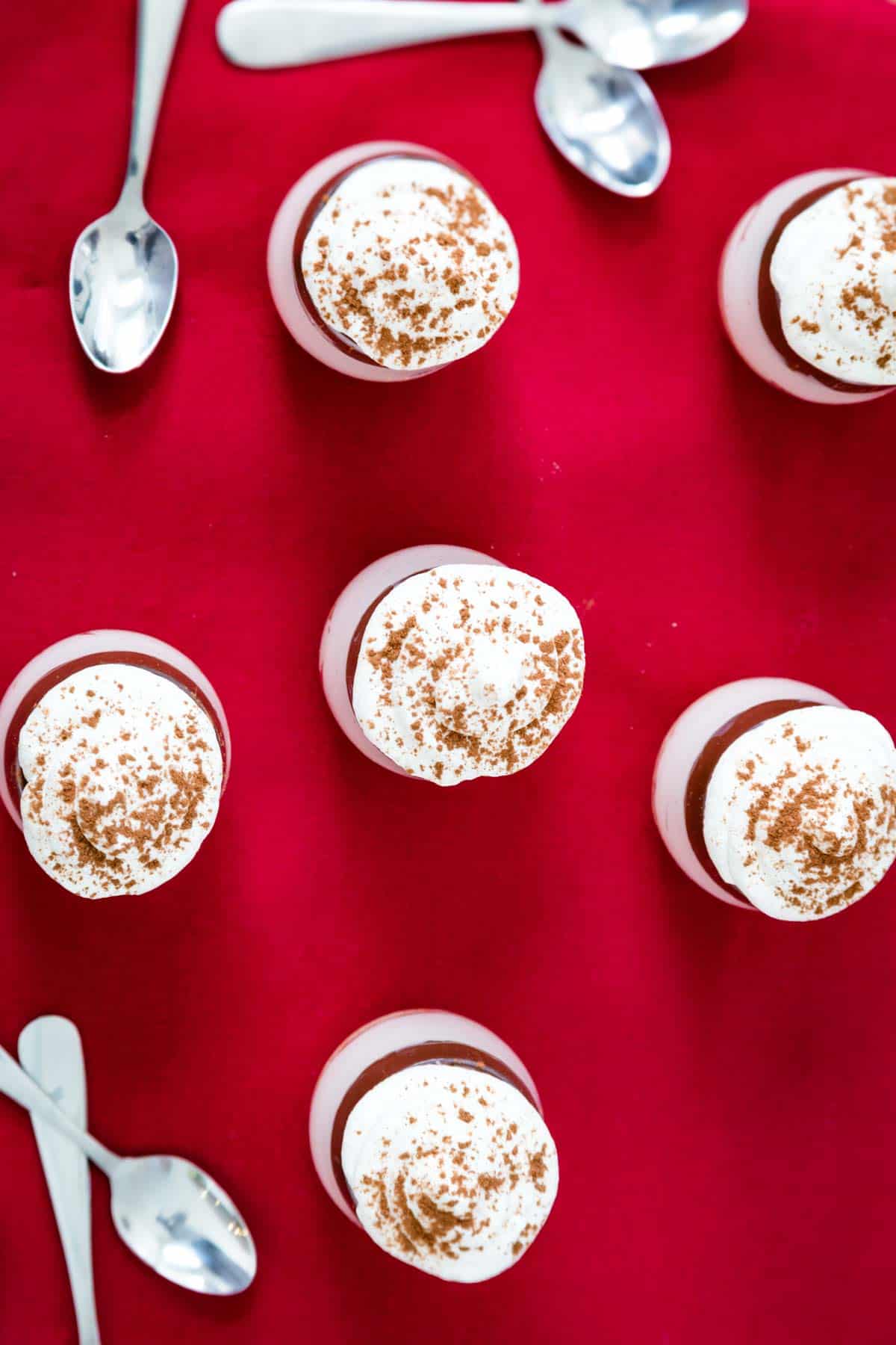 An overhead view of mini cheesecake cups topped with whipped cream and a dusting of cocoa powder on a red napkin.