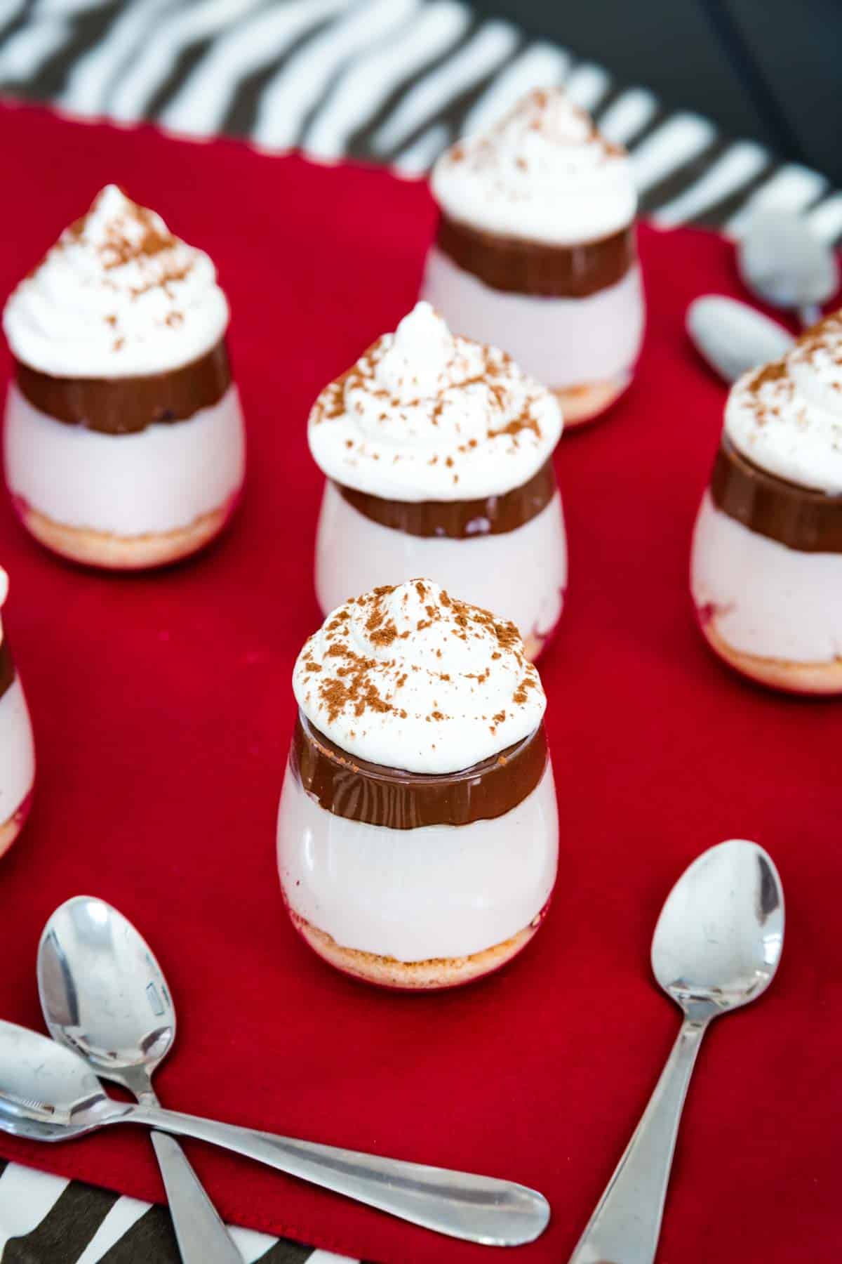 Several mini Nutella cheesecake cups on a table on top of cloth napkins with some scattered small spoons.