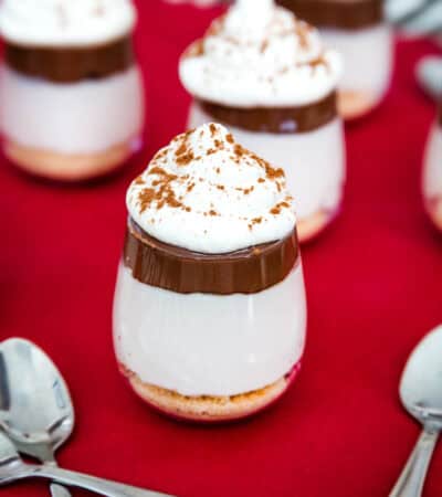 A few mini cheesecake parfaits with a Nutella layer and whipped cream on top.