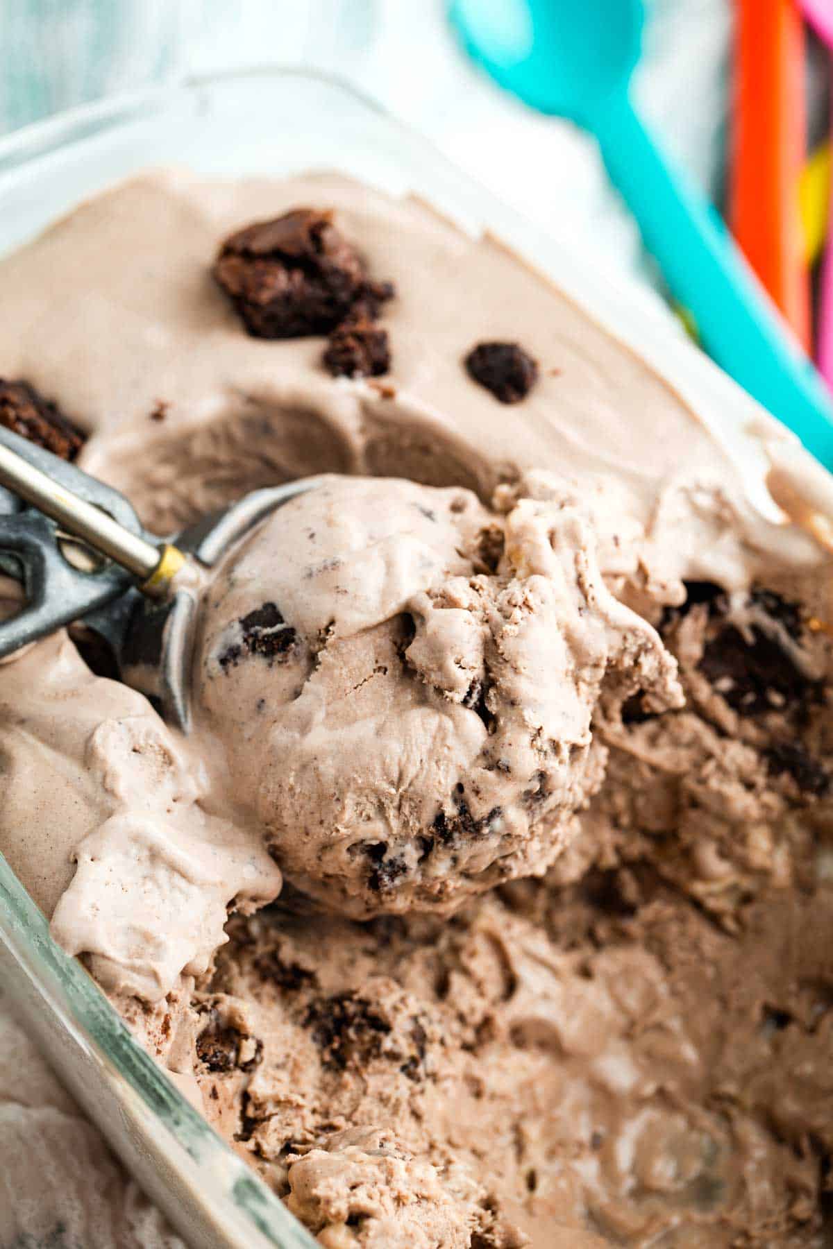 Lusciously creamy no-churn brownie batter ice cream is studded with brownie chunks and sticky bites of toasted marshmallow. An ice cream scoop digs into a container o no-churn brownie batter ice cream.