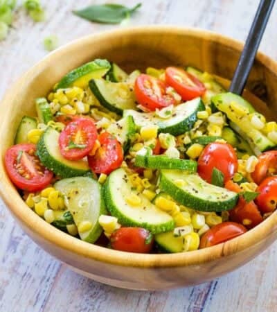 A wooden bowl full of sauteed vegetables and a serving spoon.