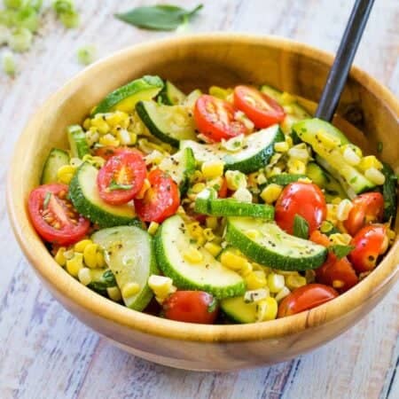A wooden bowl full of sauteed vegetables and a serving spoon.