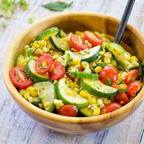 A wooden bowl full of sauteed vegetables and a serving spoon.