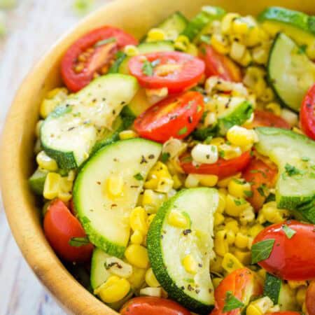 A big wooden bowl holds freshly sauteed summer vegetables.