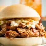 A pulled pork sandwich on a bun with text overlay that says "Slow Cooker Root Beer Pulled Pork".