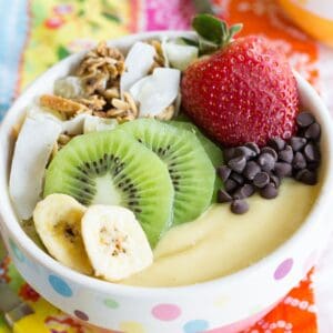 A tropical smoothie bowl topped with fruit, chocolate chips, and granola.