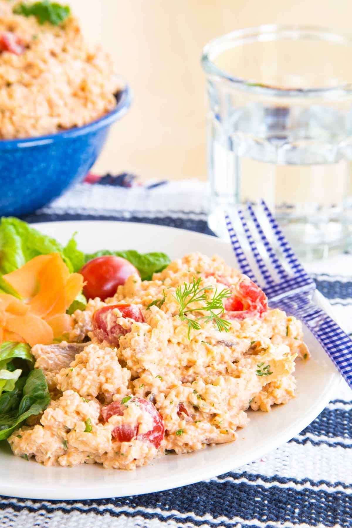 A creamy quinoa salad on a white plate with a blue fork alongside it.