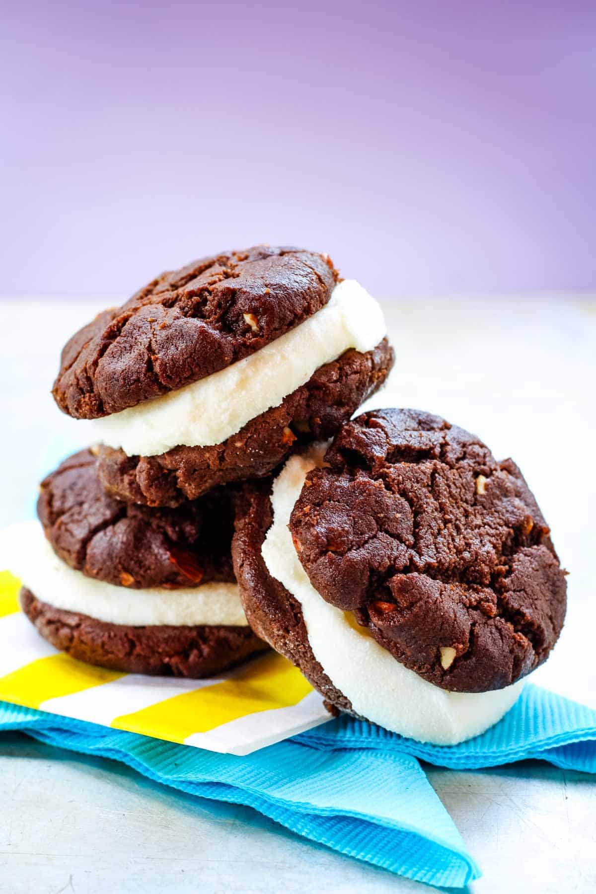 Three chocolate ice cream sandwiches piled on colorful paper napkins.