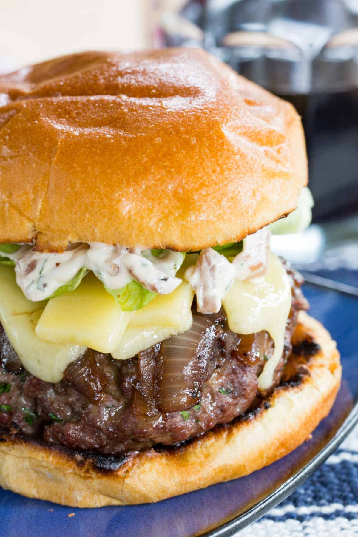 Topped with caramelized onion, gruyere, and a savory, creamy spread, these stuffed French Onion Burgers are insanely juicy and flavorful. A French onion burger on a plate.