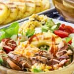 A wooden bowl of salad topped with sausage, pineapple, corn, cheese, and more with text overlay that says "Grilled Chicken Sausage Summer Salad".