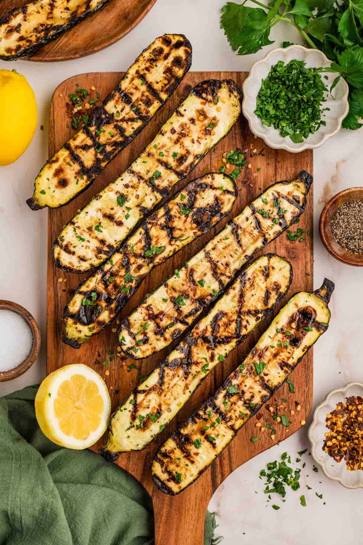 Elevate your BBQ game with this lemony grilled zucchini recipe. Lightly charred and ready in under 15 minutes, it's the perfect veggie side. Overhead image of grilled zucchini on a wooden cutting board.