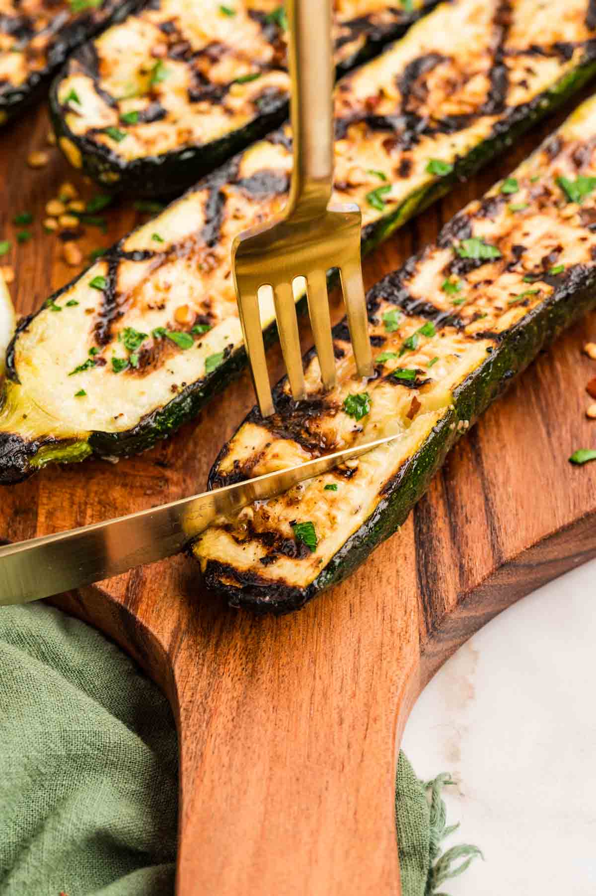 Cutting into a piece of grilled zucchini on a wooden cutting board.