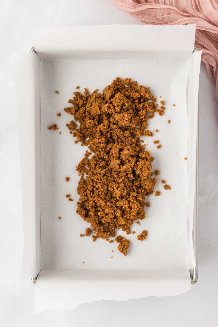 Pouring a mix of melted butter and gluten free graham cracker crumbs into a baking pan.