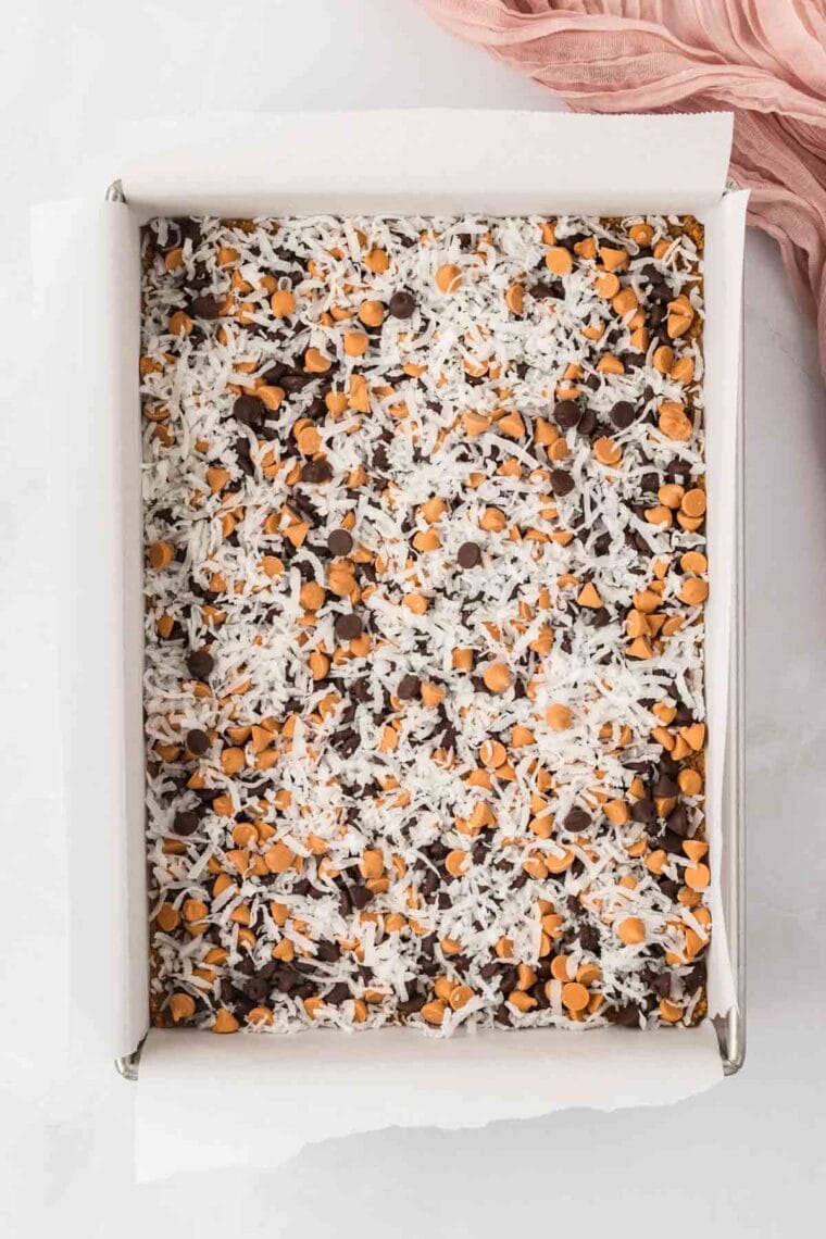 Scattering shredded coconut over a layer of chocolate and butterscotch chips for 7 layer bars.