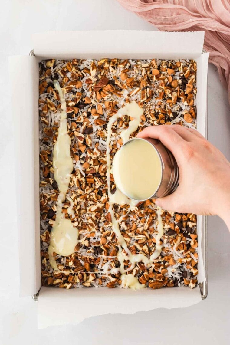 Drizzling sweetened condensed milk over 7 layer bars.