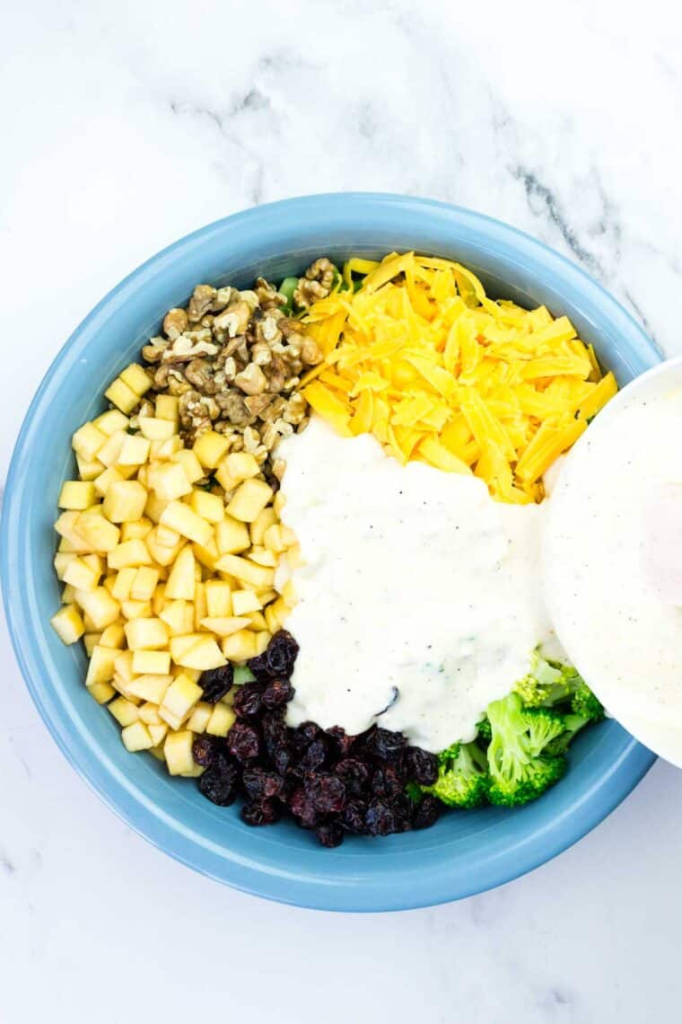 Pouring dressing over ingredients for broccoli apple salad in a bowl.