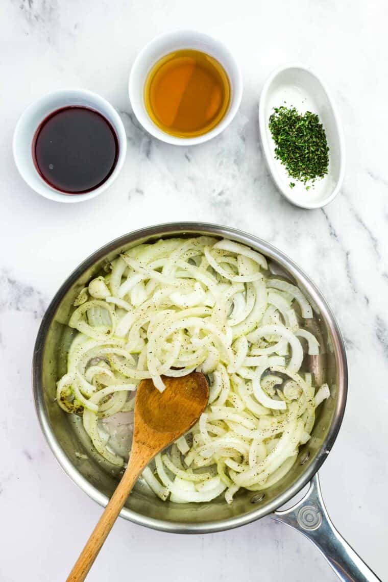 Caramelizing onions in a skillet with broth, red wine, and thyme nearby.