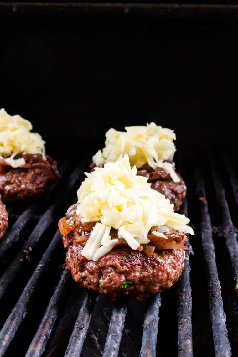 Topping grilling burgers with gruyere cheese.