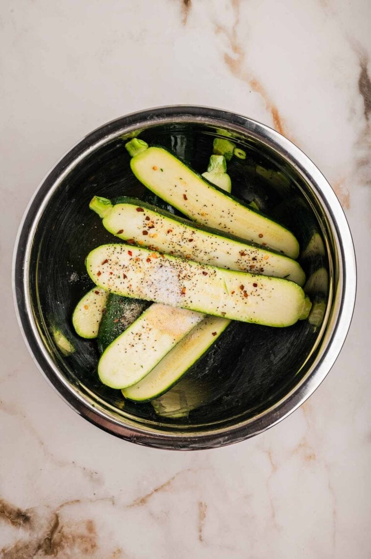 Adding olive oil, lemon juice, and seasoning to zucchini in a bowl.