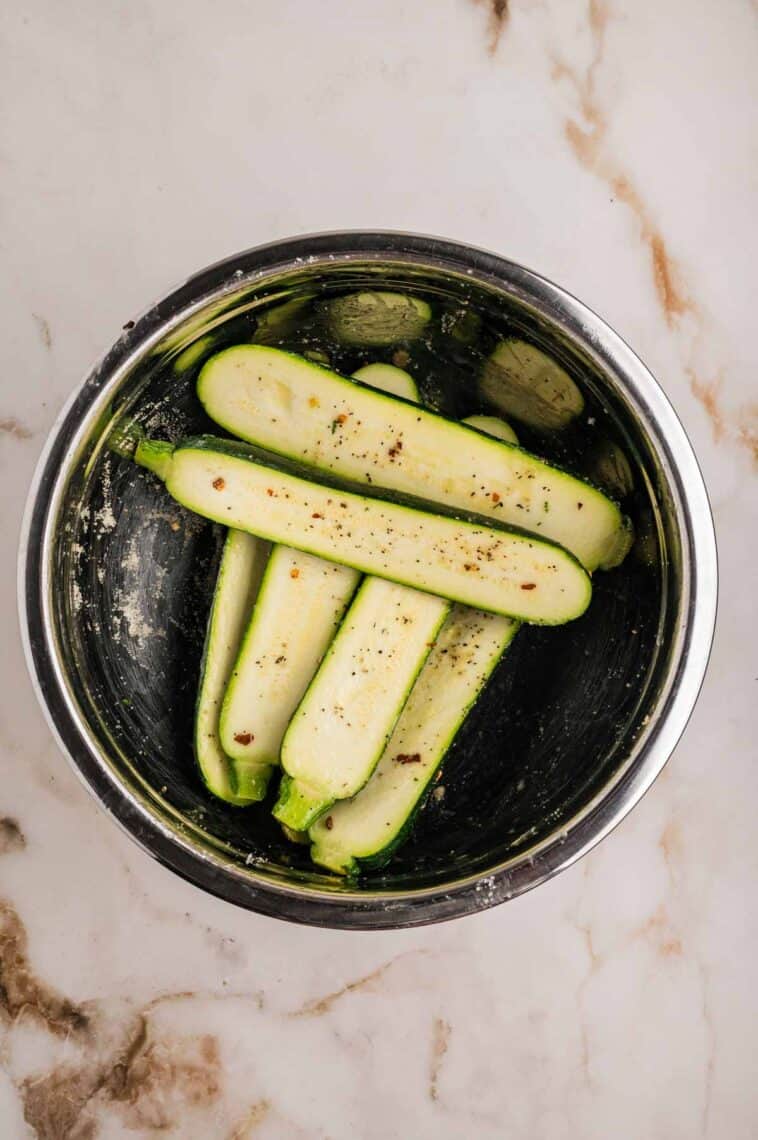 Zucchini tossed in olive oil, lemon juice, and seasoning in a bowl.