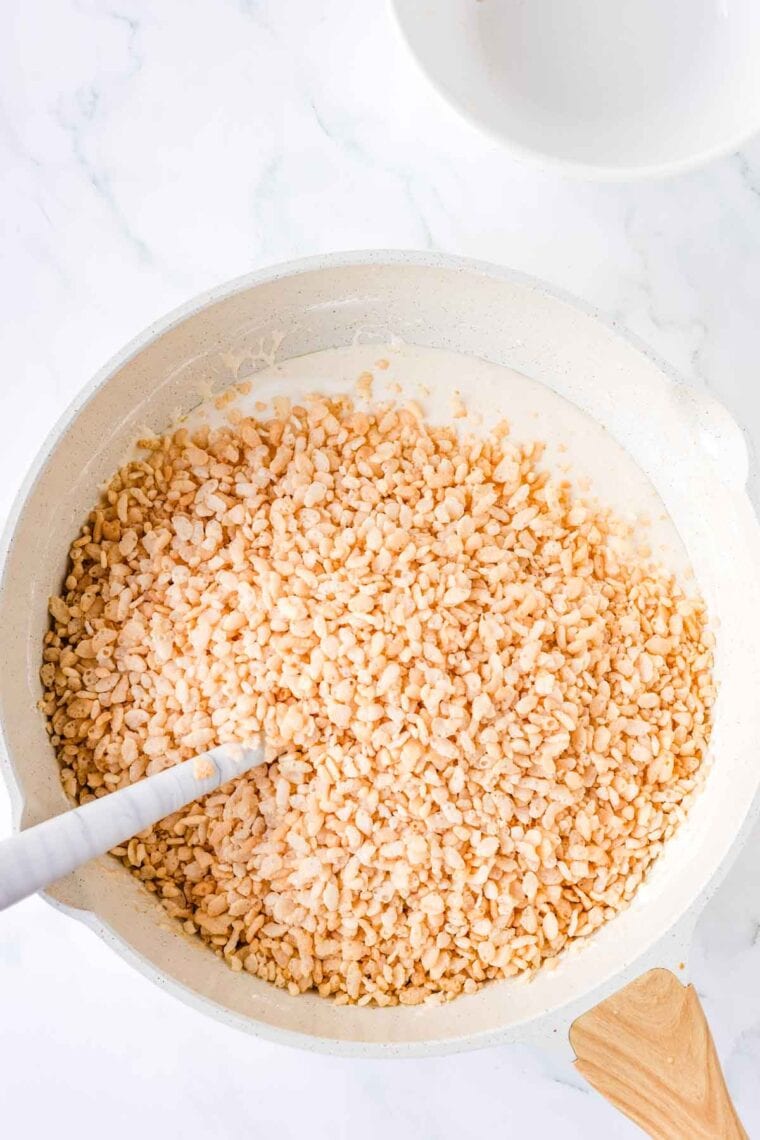Adding crispy rice cereal to a Dutch oven full of melted butter and marshmallow fluff.