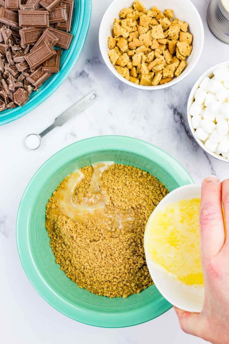 Pouring butter over graham cracker crumbs.