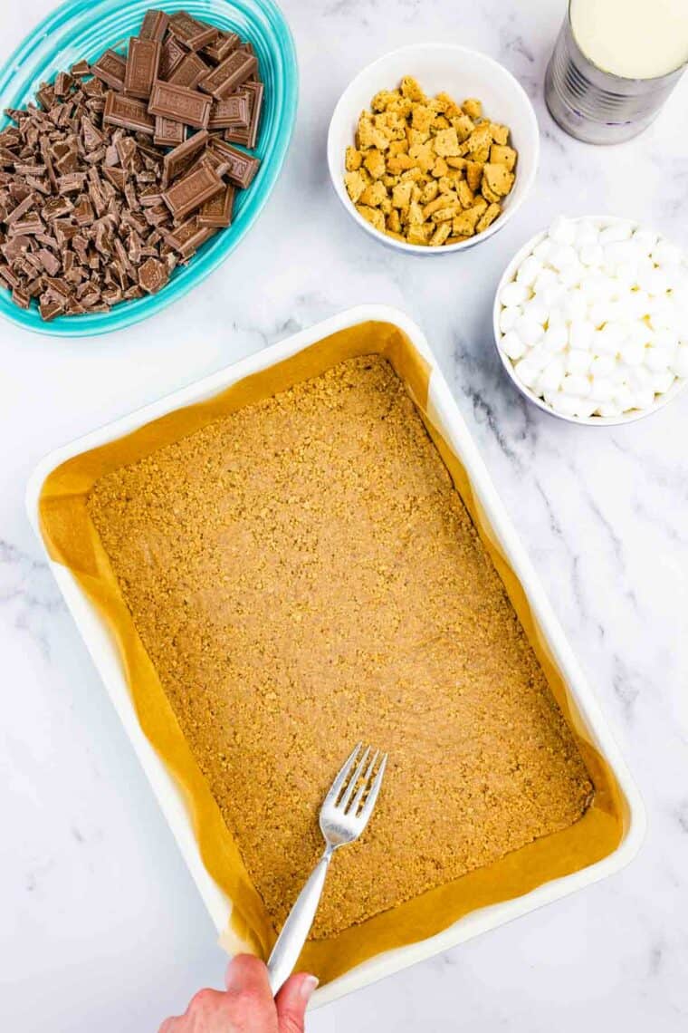 Using a fork to press graham cracker crust into the bottom of a baking pan.