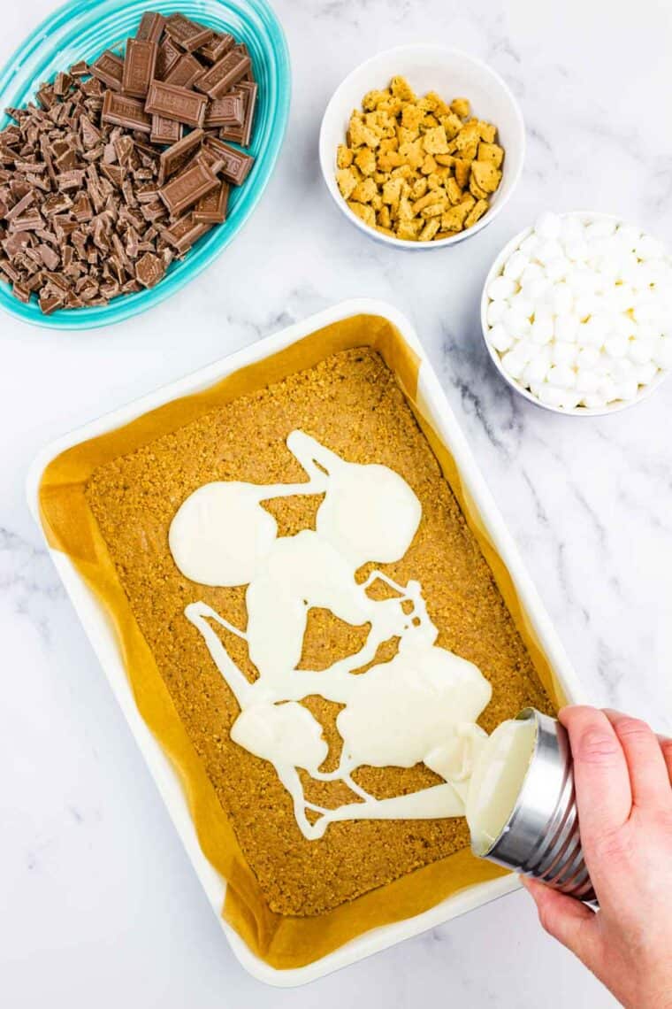 Pouring sweetened condensed milk over a graham cracker crust.