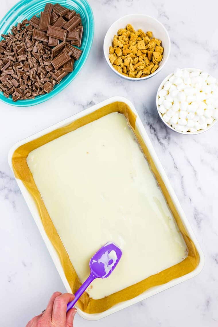 Spreading sweetened condensed milk over a graham cracker crust.