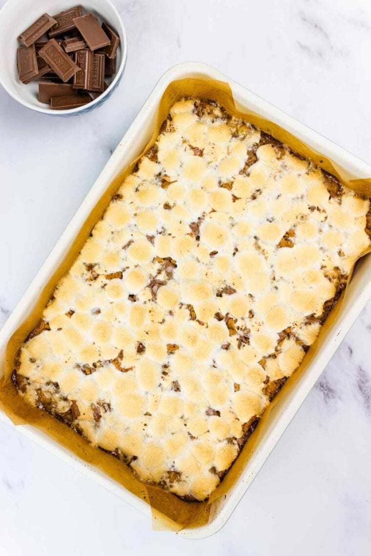 S'mores bars fresh out of the oven next to a bowl of Hershey's chocolate pieces.